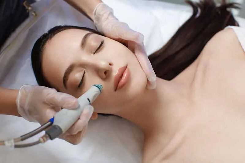 A close-up view of a person receiving a Hydrafacial treatment, with a specialized handheld device gently cleansing and exfoliating their skin.