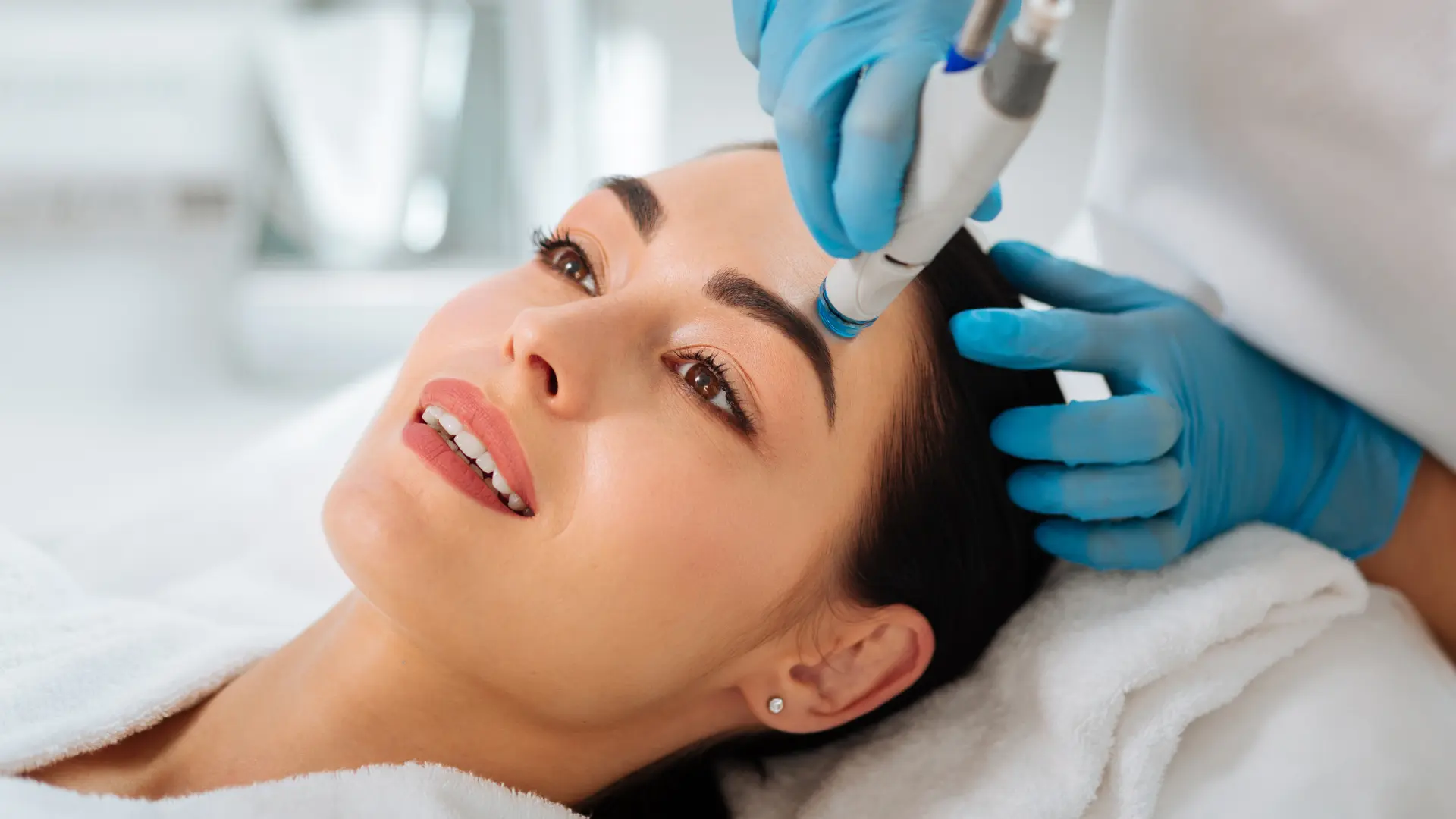 A close-up image of a HydraFacial booster serum being applied to a person's face during a spa treatment.